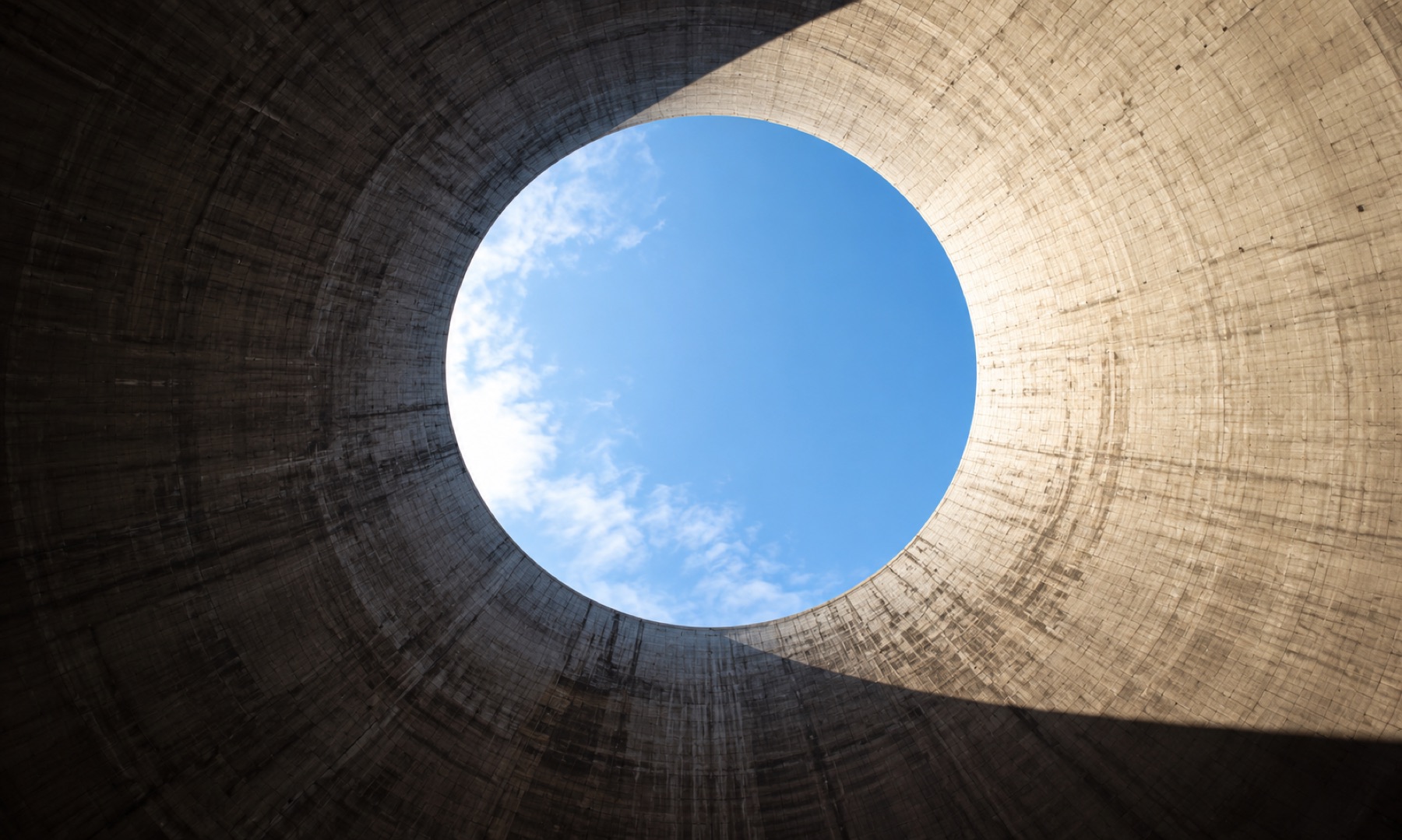 Looking up through the circular opening of a concrete cooling tower to blue sky