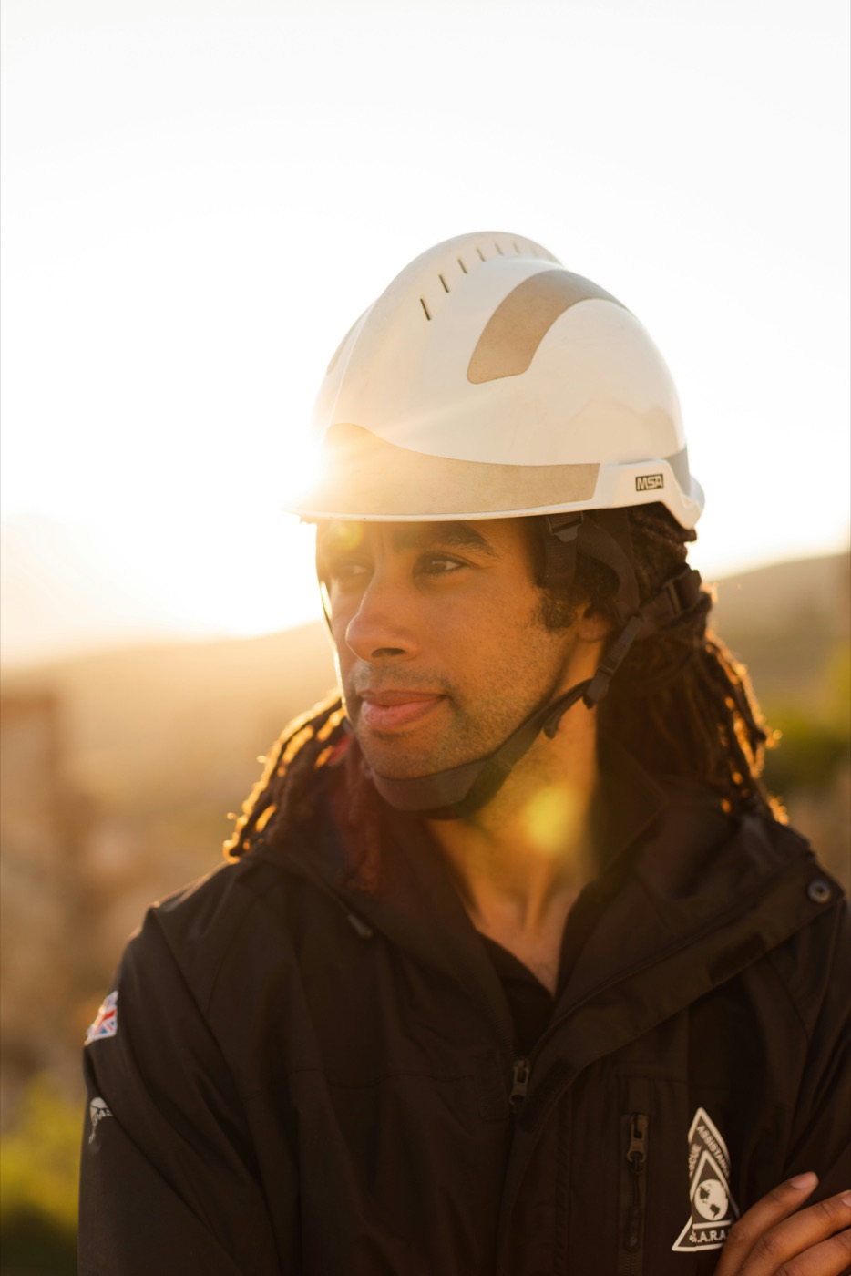 Engineer in a white hard hat, backlit at golden hour