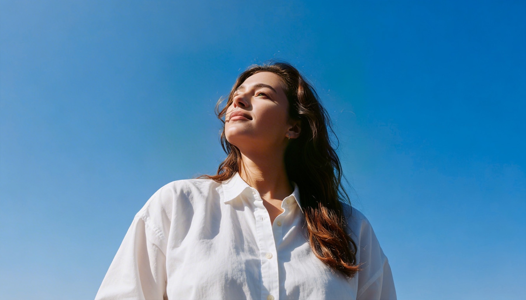 Woman in a white shirt photographed from below against deep blue sky